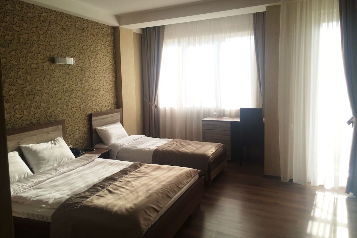 A hotel room with two beds, a desk, and a window with curtains.