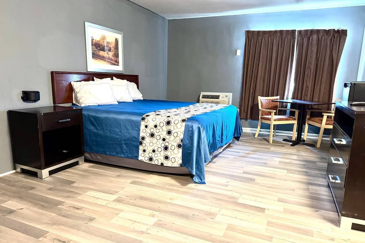 Quarto de hotel com cama, escrivaninha, cadeira, televisão e um quadro na parede.