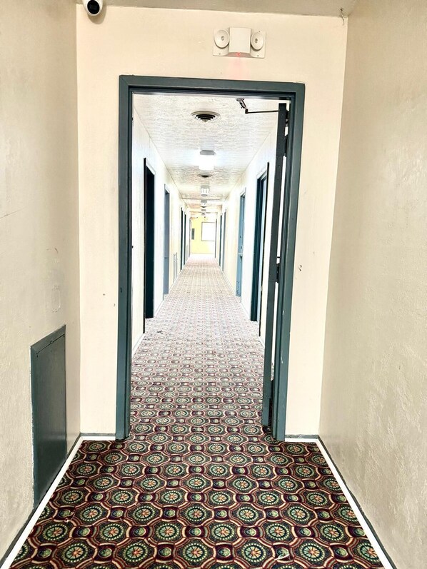 Un long couloir au sol décoré de motifs, avec des portes de chaque côté et un plafond orné de luminaires.