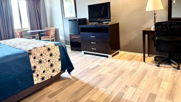 Habitación de hotel con cama, escritorio, silla, televisión y lámpara.
