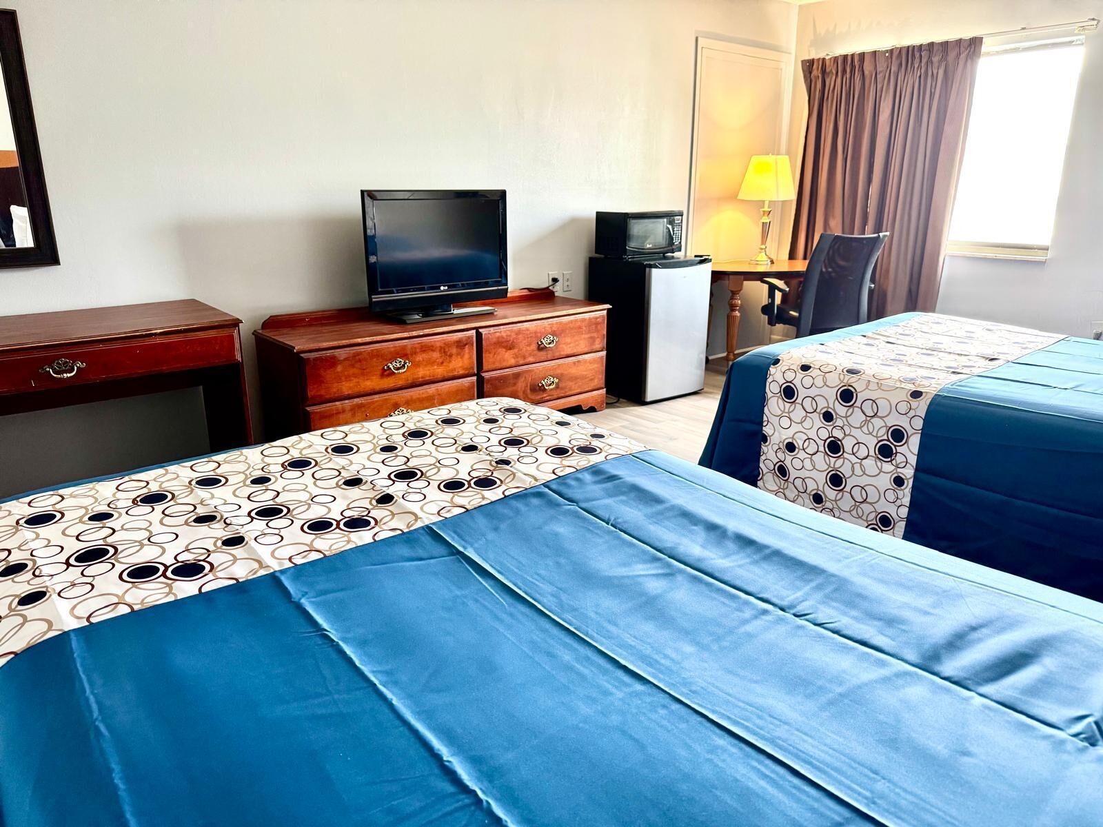 Habitación de hotel con dos camas, televisor, escritorio con lámpara y refrigerador.