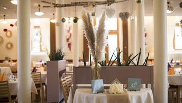 A restaurant interior with a table set for two, featuring a vase with pampas grass, a small house-shaped decoration, and a menu card.