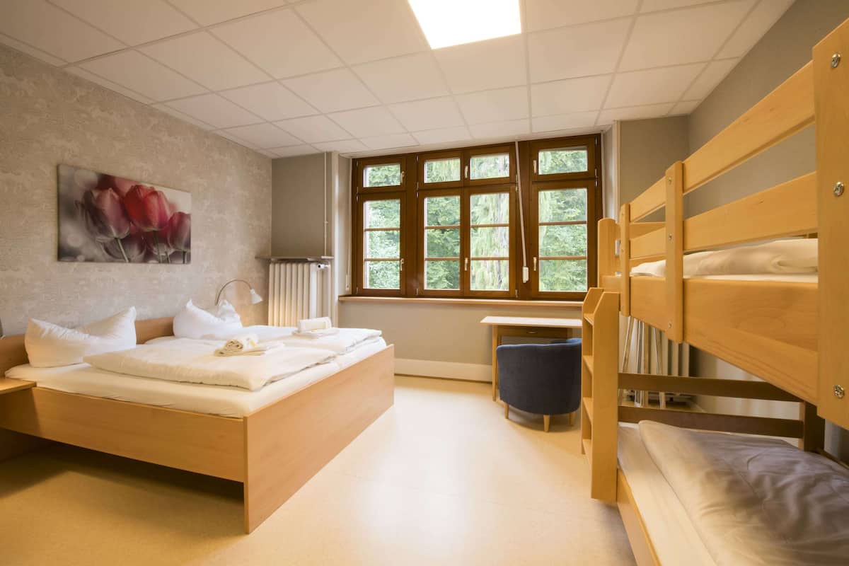 A bedroom with a wooden bed, a desk, and a window with a view of trees.