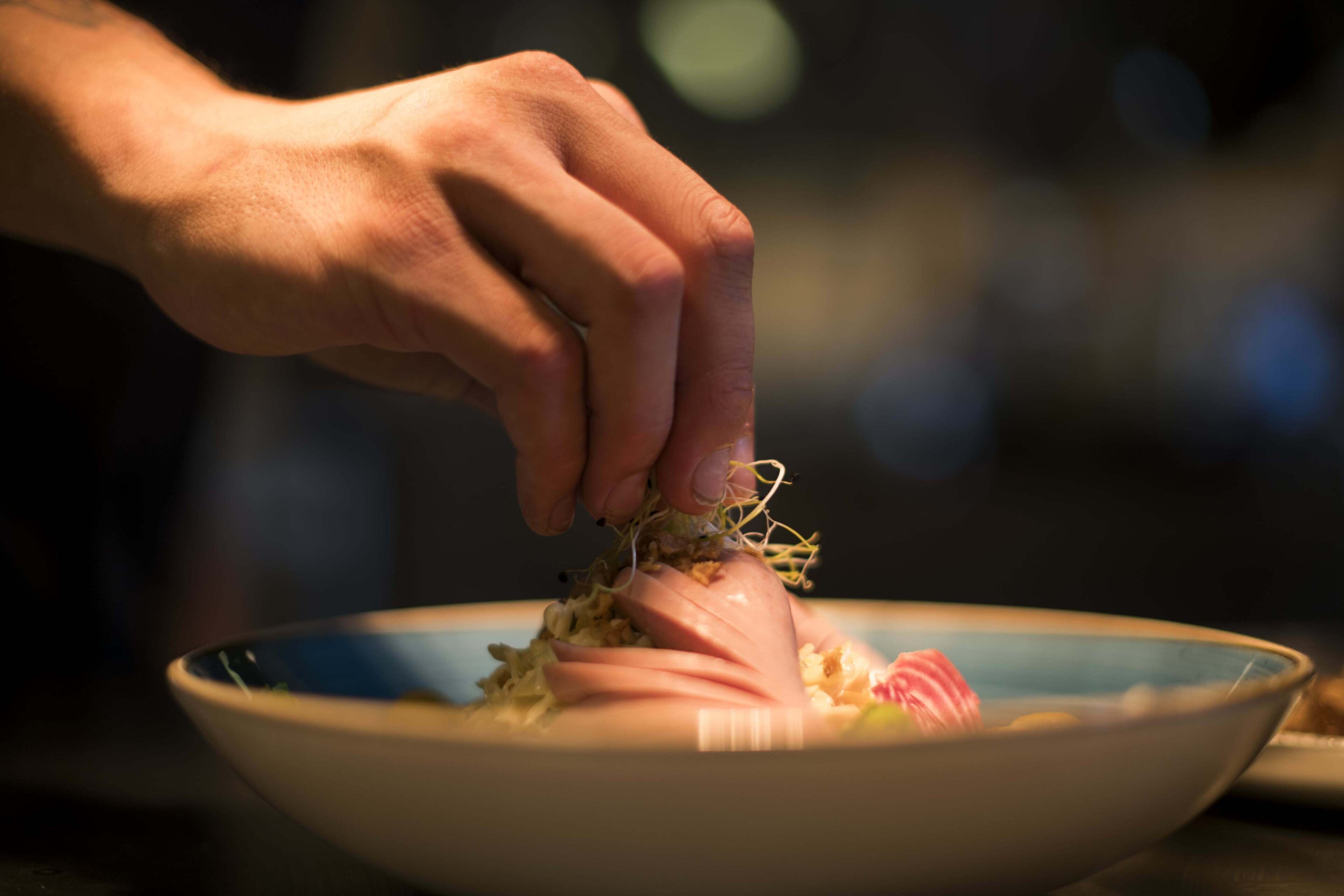 A hand holding a piece of food over a bowl.