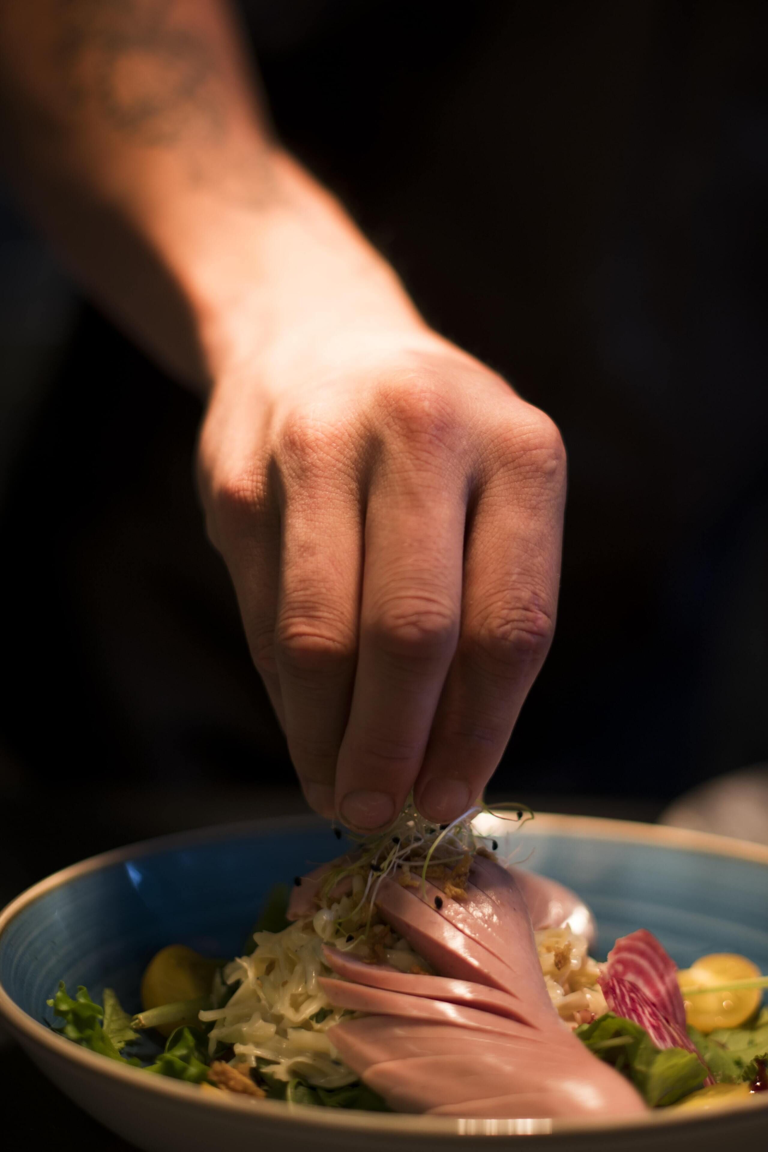 A hand holding a fork over a bowl of salad with various vegetables and a piece of meat.