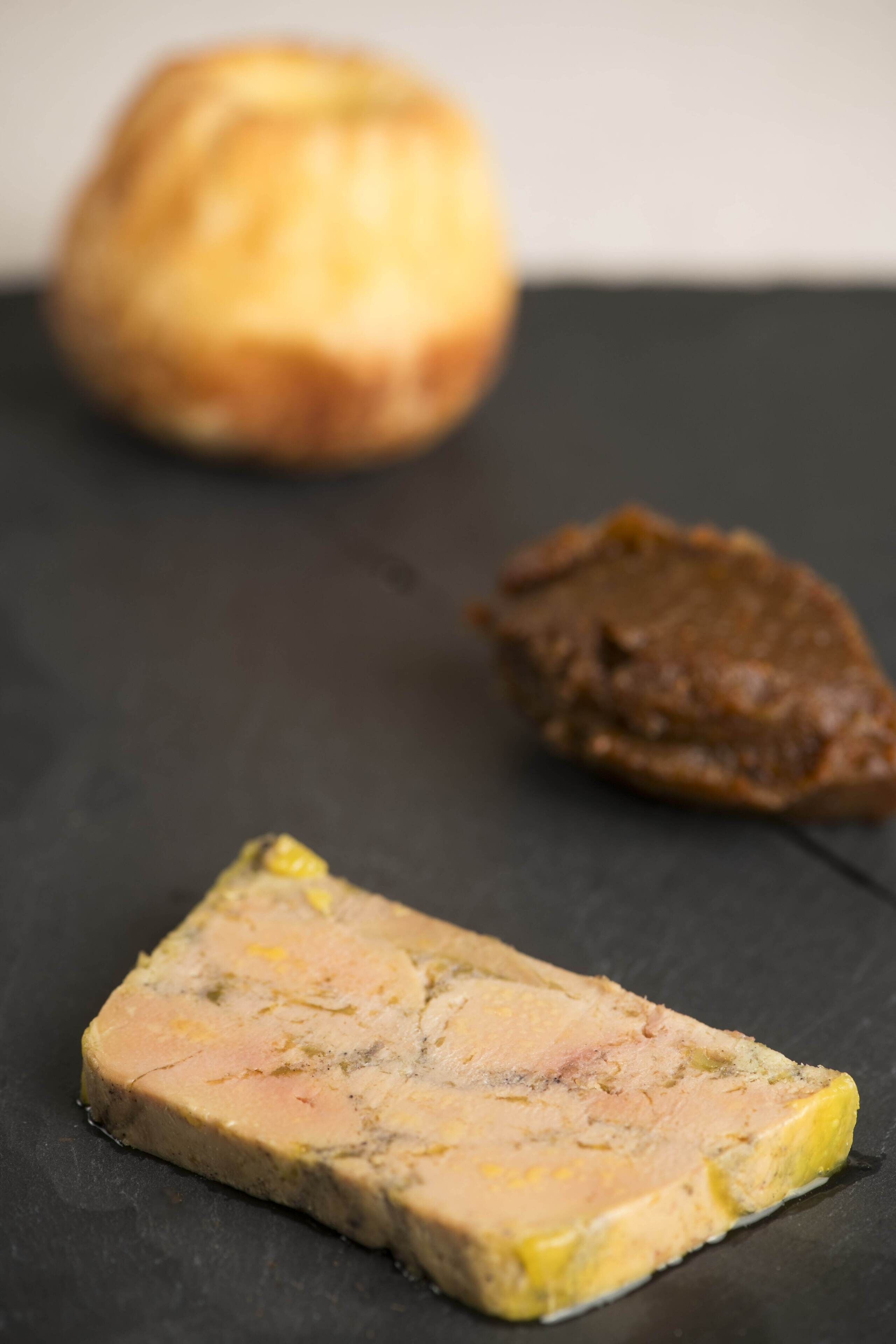 A slice of terrine and a piece of pâté on a slate surface.