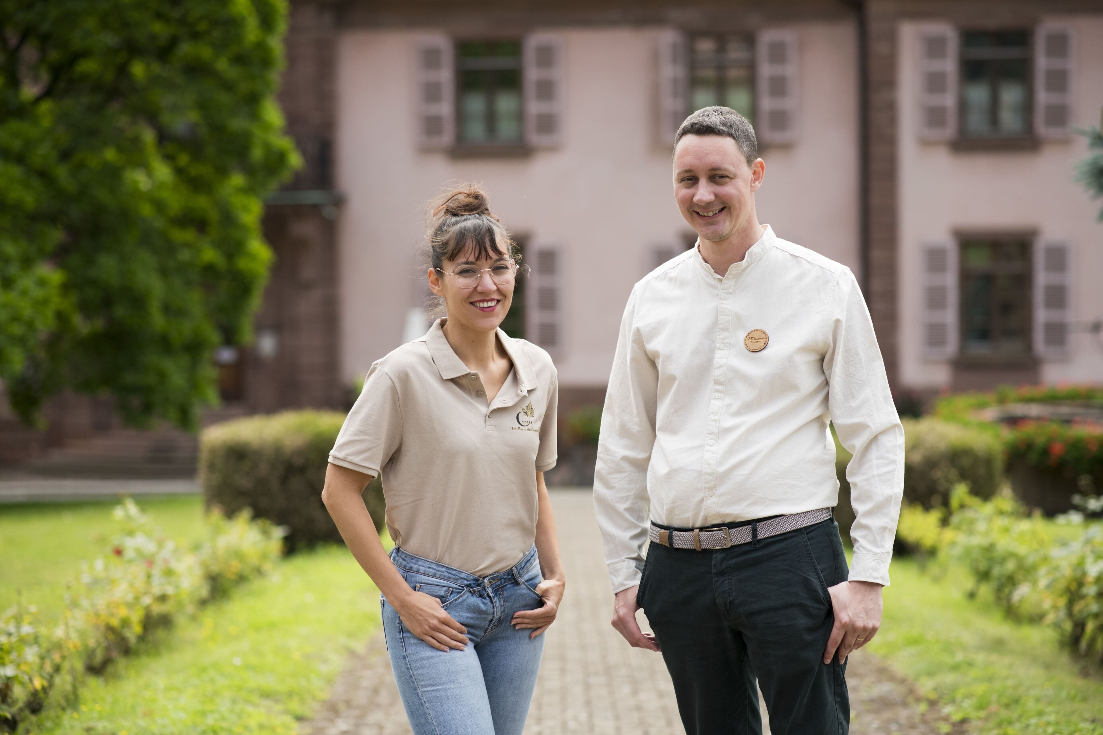 Un homme et une femme se tiennent debout dans un jardin, avec un bâtiment en arrière-plan.