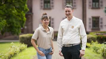A man and woman standing in a garden with a building in the background.