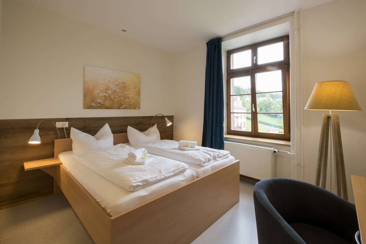 A hotel room with a large bed, bedside tables, a lamp, a chair, and a window with curtains.