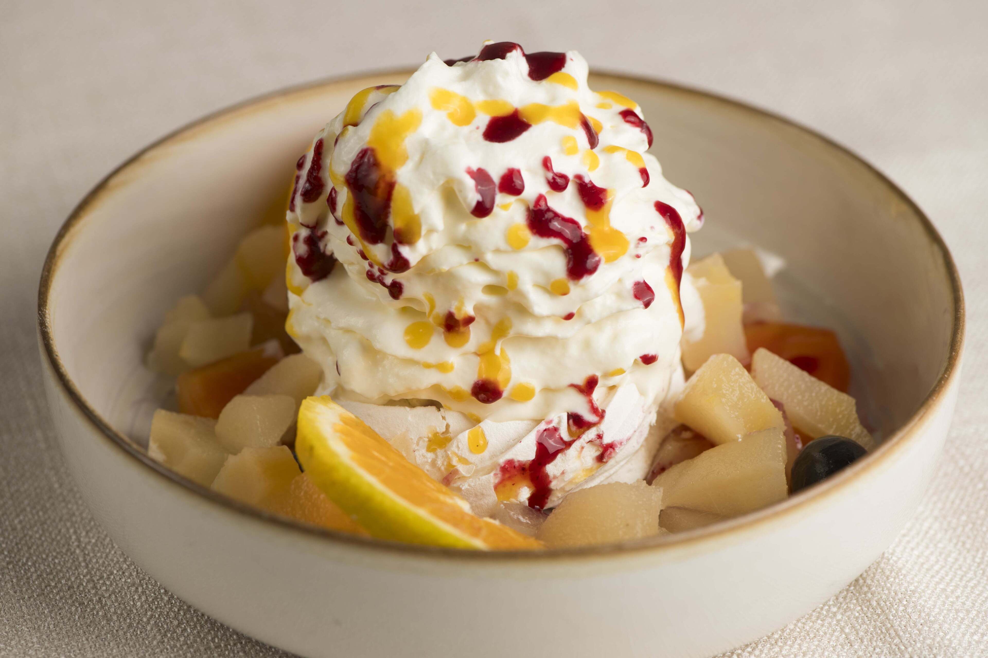 A bowl of dessert with fruit and whipped cream.