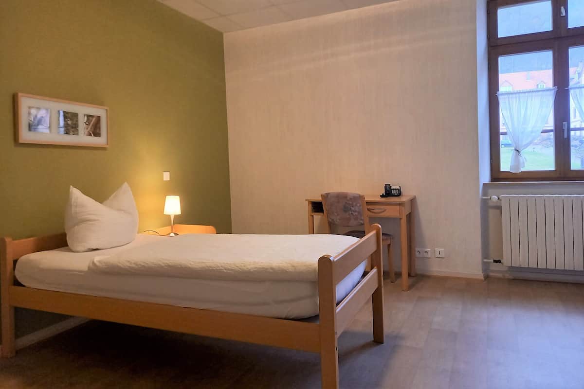 A bedroom with a bed, bedside table, lamp, chair, and a window with a view.