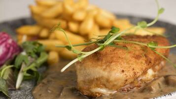 A plate with a breaded and fried item, possibly a fish fillet, accompanied by golden fries and a side of greens.
