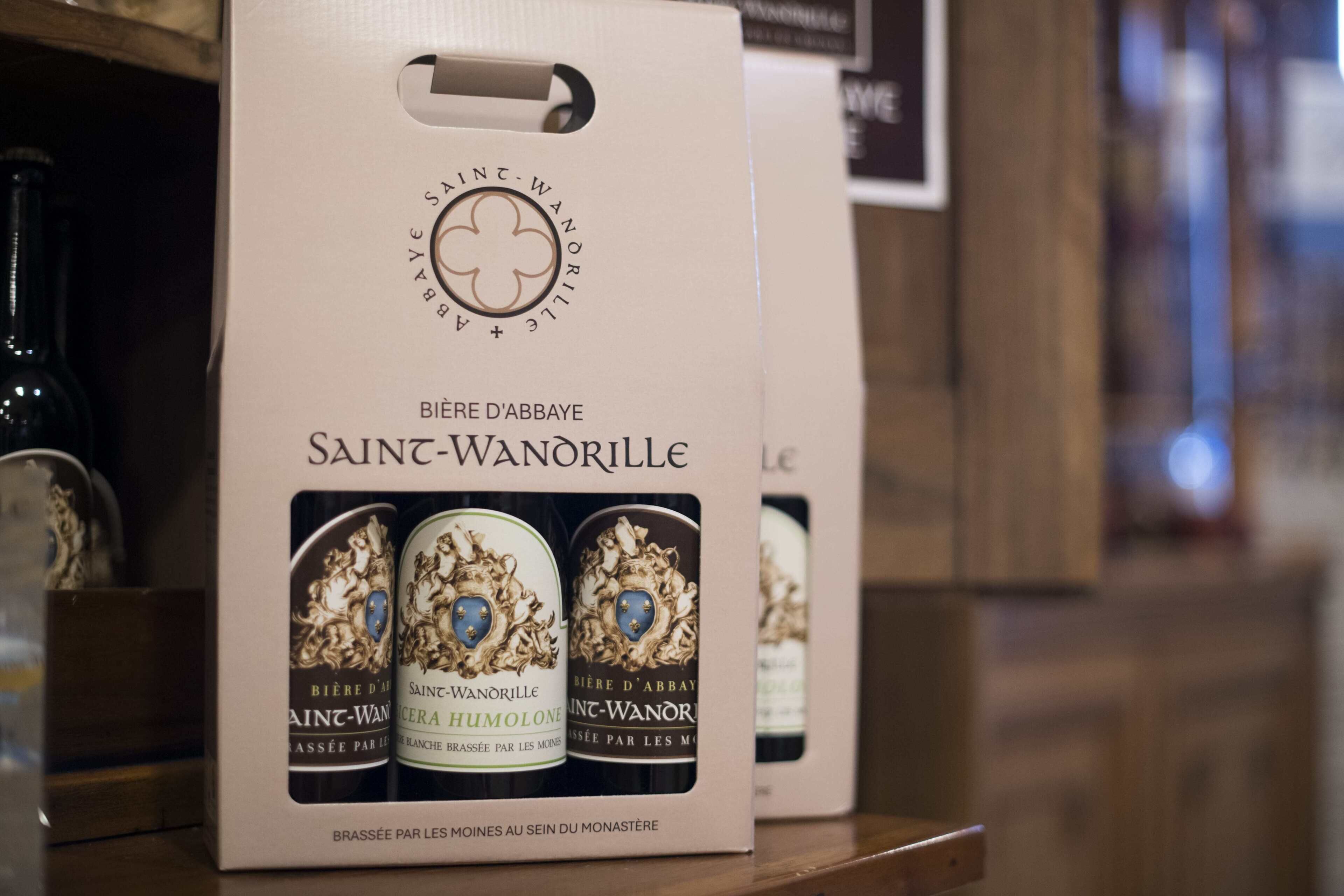 Una caja de vino Saint-Wanorille con un logotipo de trébol y texto que indica que es elaborado por monjes en el monasterio.