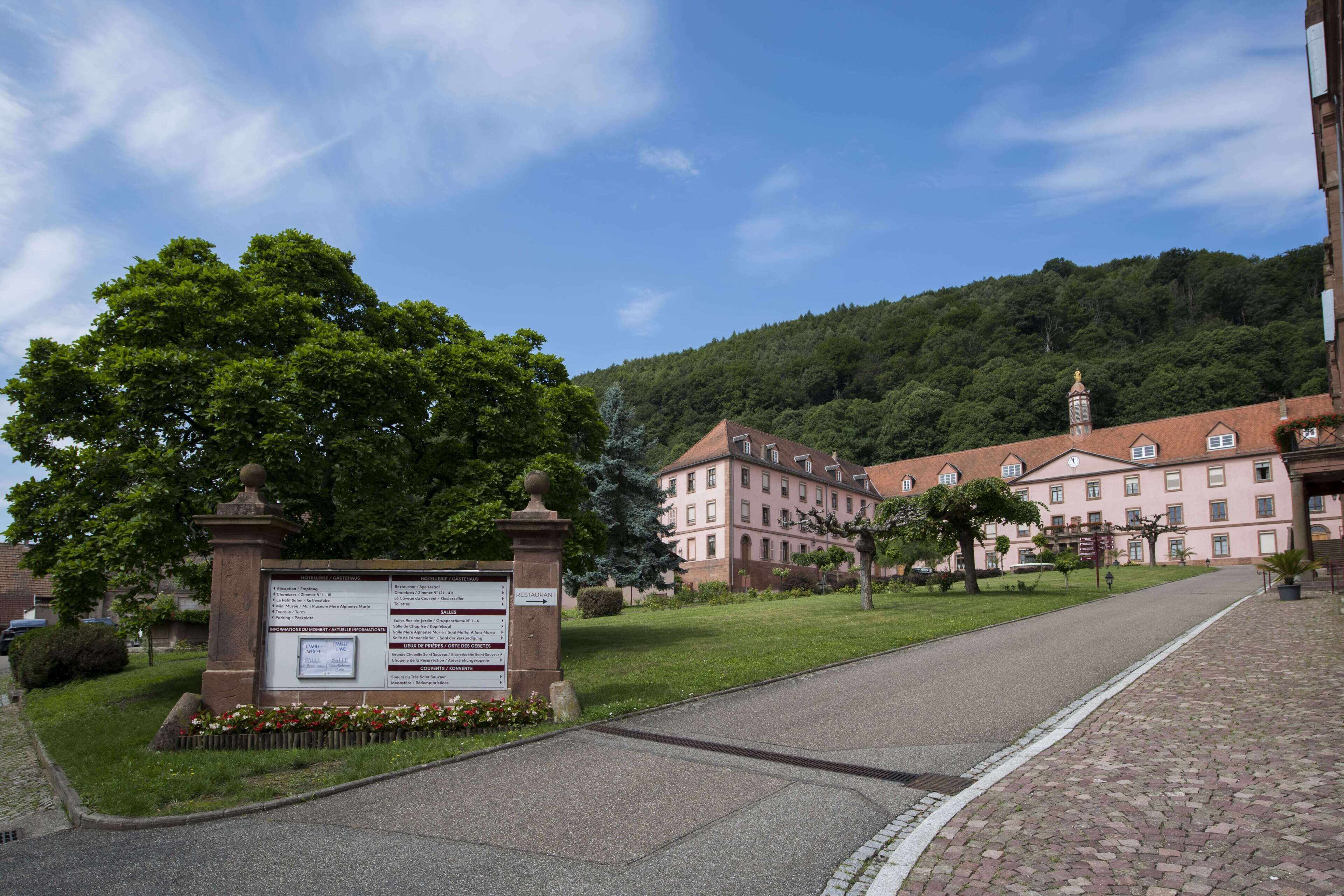 A building with a paved entrance, a signboard, and a grassy area with trees.