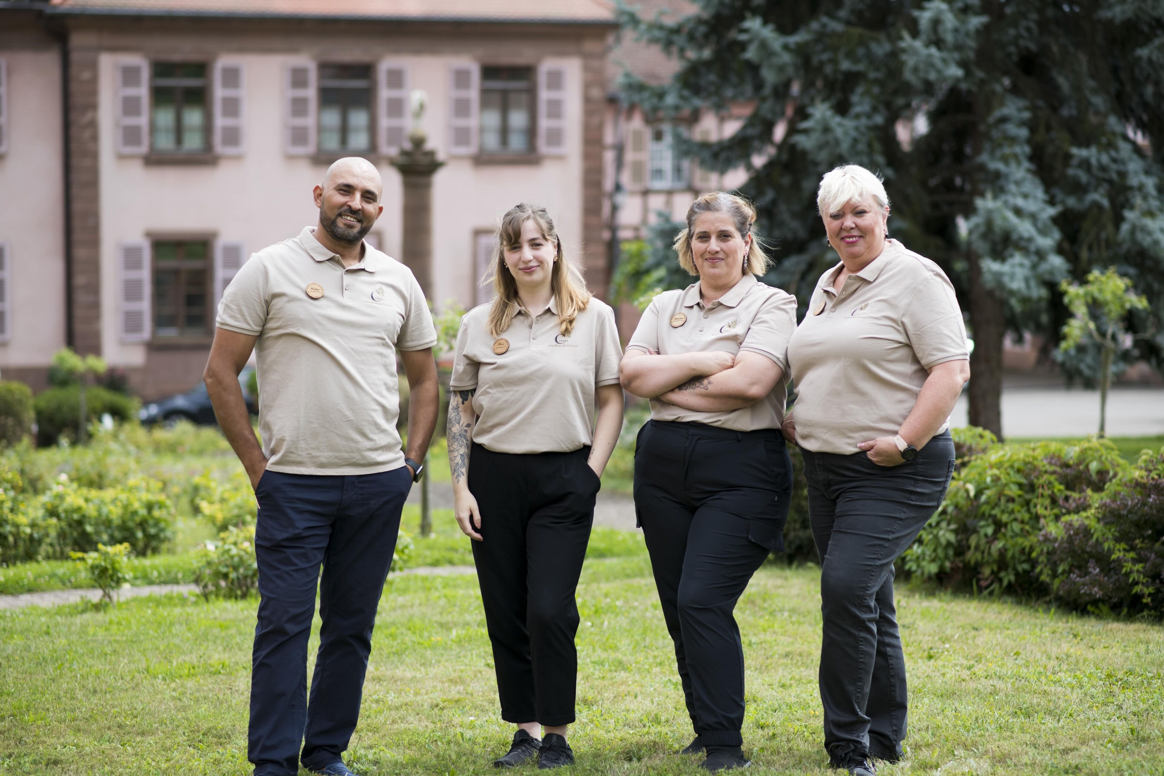 Cuatro personas de pie en un área verde con un edificio al fondo.