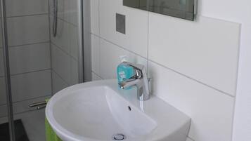 Ein Badezimmer mit Duschkabine aus Glas, einem weißen Waschbecken und einem Spiegel.