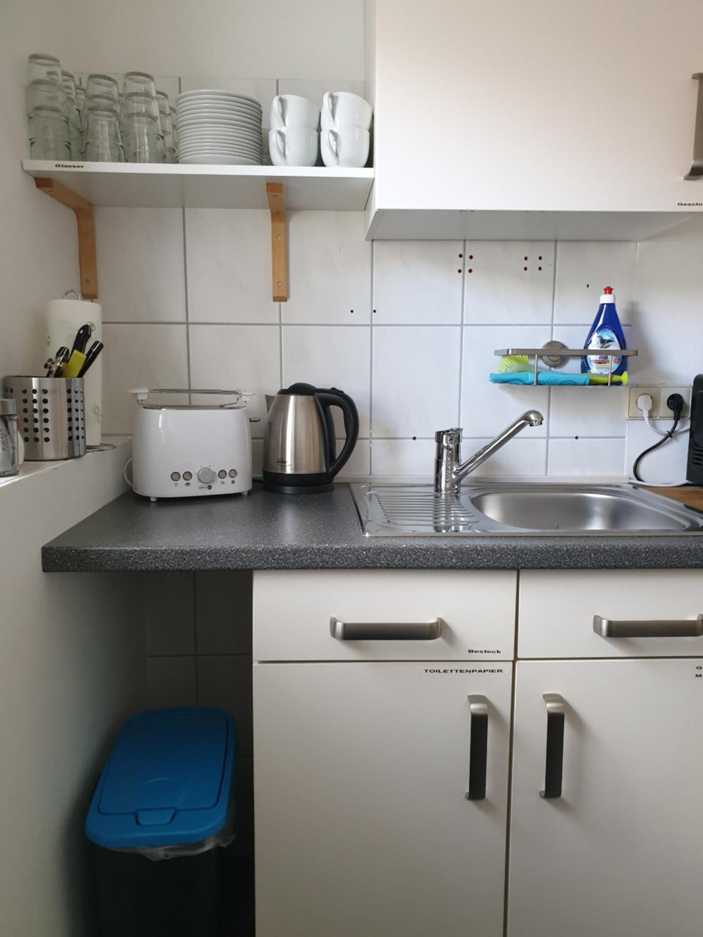Una cocina compacta con armarios blancos, una encimera negra, un fregadero y una cafetera.