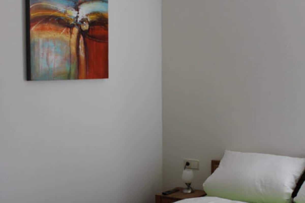 A bedroom with a bed, green bedding, a nightstand, a lamp, and a painting on the wall.