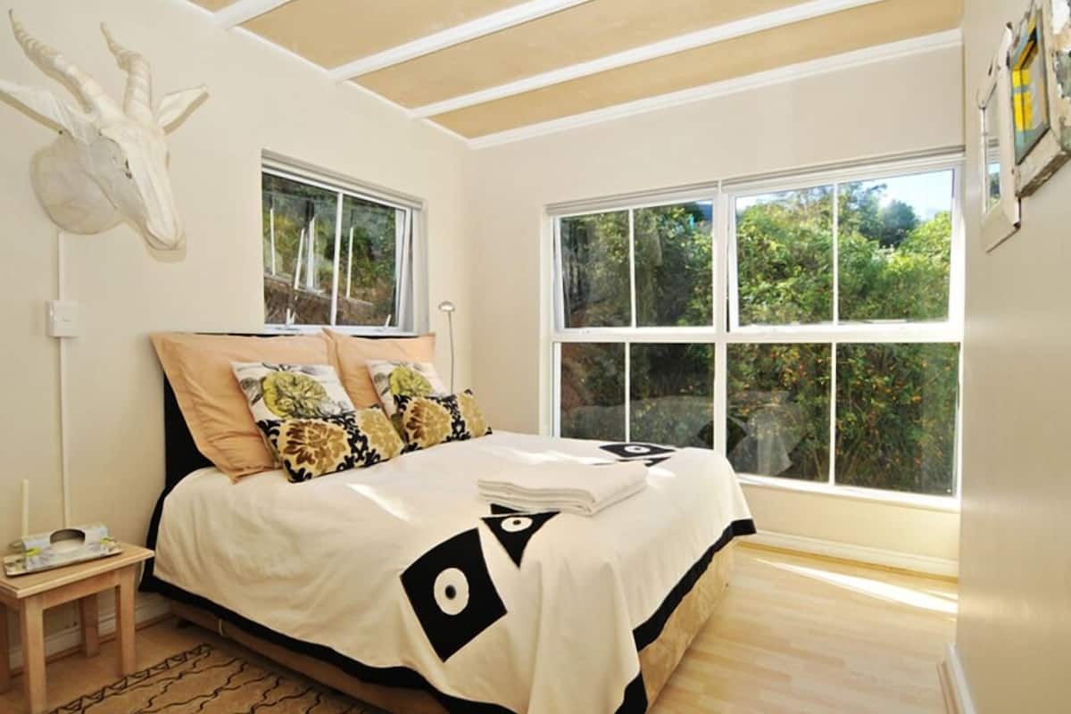 A bedroom with a bed, two windows, a mounted animal head, and a small bedside table.