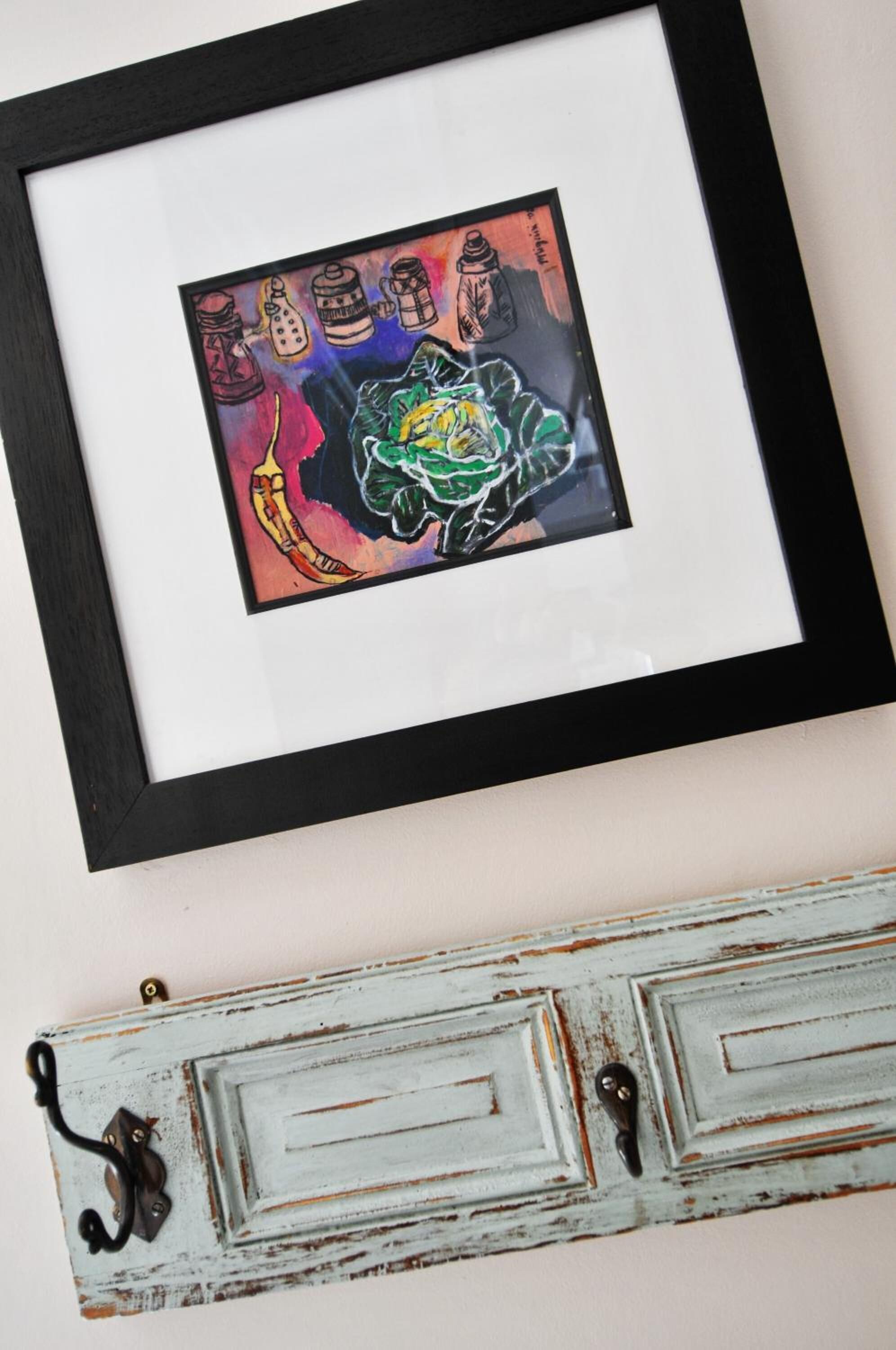 A framed artwork with a colorful abstract design, mounted on a wall above a rustic, distressed wooden shelf.