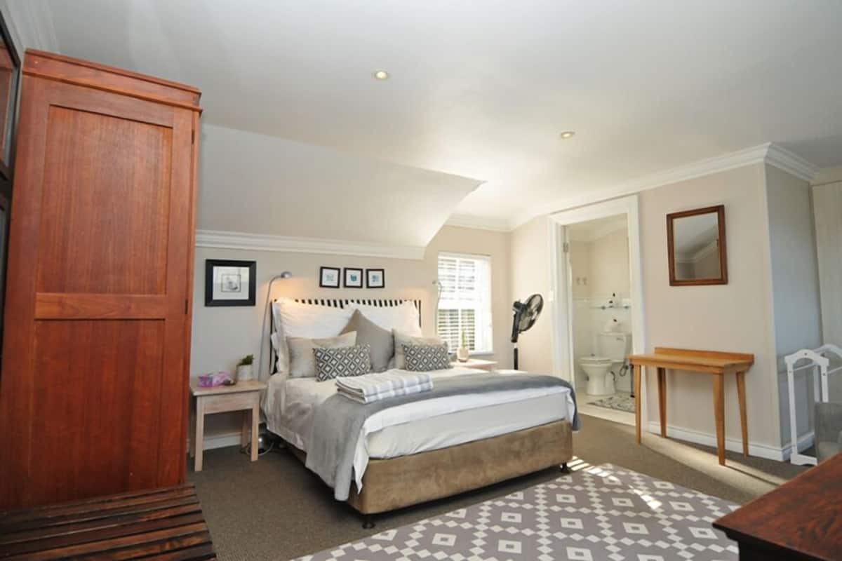 A bedroom with a bed, bedside tables, a wooden wardrobe, a mirror, and a window with blinds.