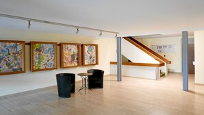 Ett konstgalleri med abstrakta målningar, en trappa och en sittgrupp med ett litet bord.