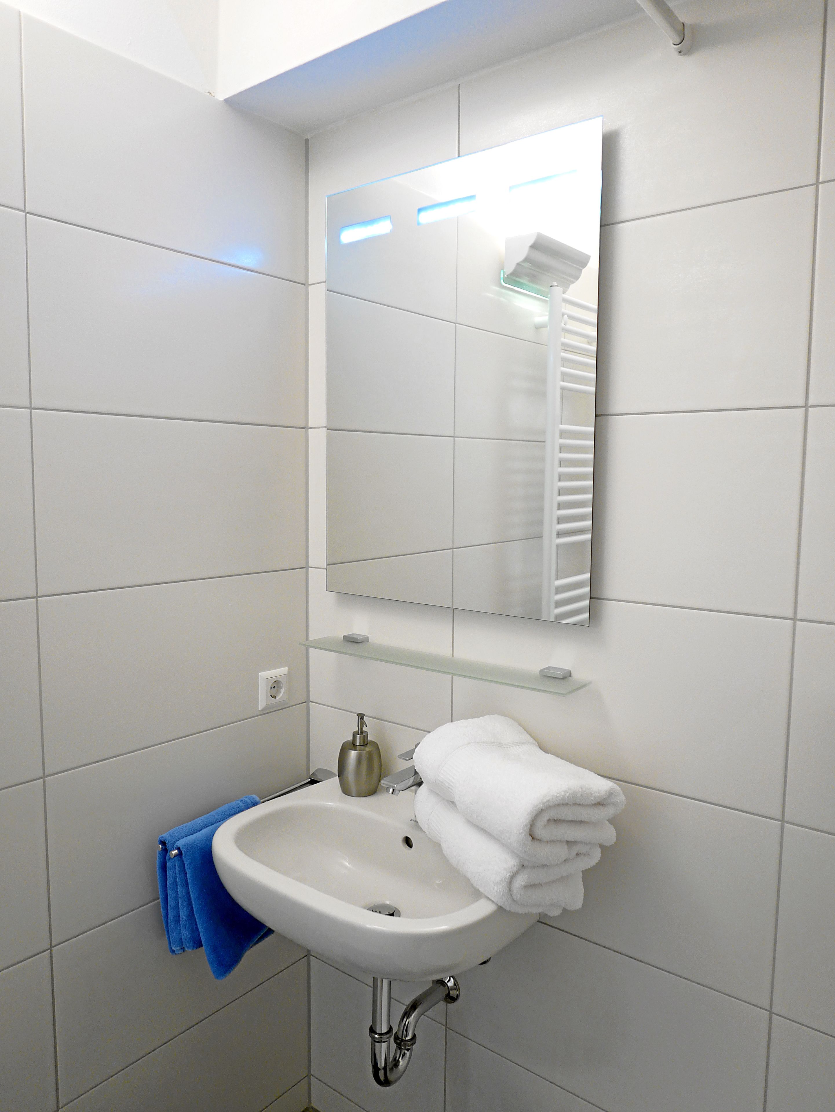 Un bagno con un lavandino bianco, uno specchio e un porta asciugamani.