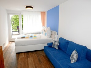 A bedroom with a bed, a blue sofa, a window with curtains, and a radiator. - Apartment Moewe (Meersburg)