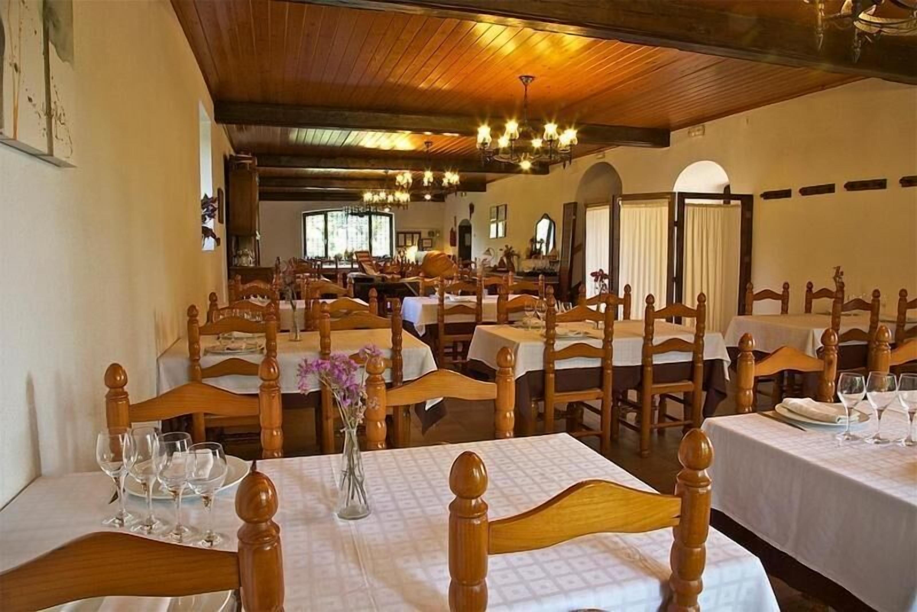 A dining area with wooden tables and chairs, arranged in a spacious room with high ceilings and chandeliers.