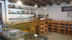 A bar area with wooden chairs and stools, shelves with bottles, and a coffee machine.