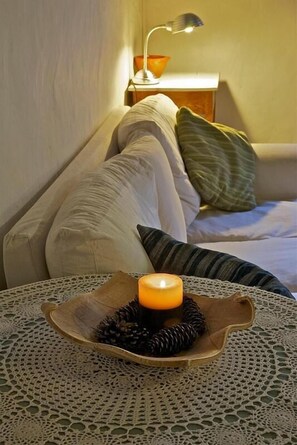 A cozy room with a lit candle on a lace table, a sofa with cushions, and a lamp in the background. - Hostal Falgars (La Pobla de Lillet)