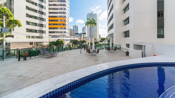 A rooftop pool area with lounge chairs, a palm tree, and high-rise buildings in the background. - Excelente flat em Setúbal, Boa Viagem 1Q 3 pessoas. Conforto e ótima localização PM802 (Recife)
