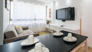 A modern living room with a black dining table set for four, a sofa, a TV mounted on the wall, and a potted plant. - Excelente flat em Setúbal, Boa Viagem 1Q 3 pessoas. Conforto e ótima localização PM802 (Recife)