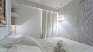 A neatly made bed with white linens and rolled towels, a wooden headboard, and a wall with a geometric pattern. - Excelente flat em Setúbal, Boa Viagem 1Q 3 pessoas. Conforto e ótima localização PM802 (Recife)