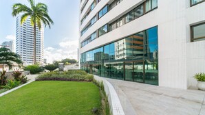 A modern building with large windows, a well-maintained lawn, and a tall palm tree. - Excelente flat em Setúbal, Boa Viagem 1Q 3 pessoas. Conforto e ótima localização PM802 (Recife)