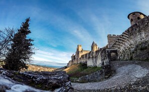 A historic stone castle with a prominent tower and battlements, a cobblestone path leading to the entrance, and a clear sky. - Art Home B&B (Carcassonne)