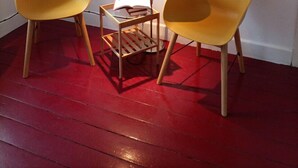Une pièce avec deux chaises jaunes, une petite table en bois sur laquelle se trouve une lampe, et une photographie en noir et blanc encadrée accrochée au mur.