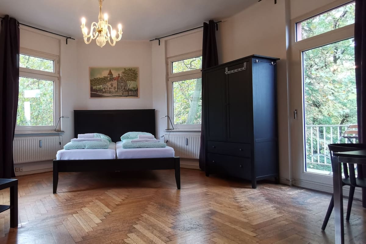 A bedroom with a bed, a desk, a chair, a wardrobe, and large windows.