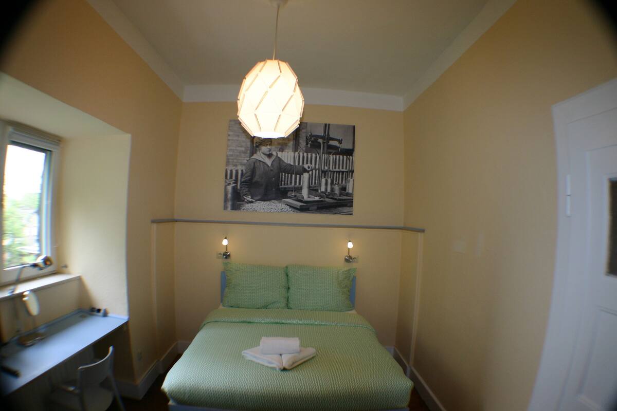 A bedroom with a bed, a desk, and a window.
