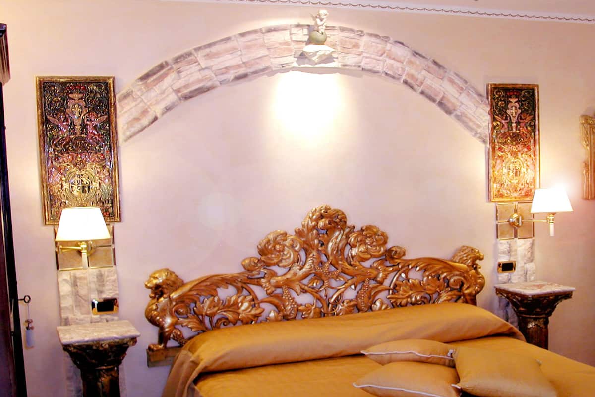 A room with a bed, two wall-mounted lamps, and a door with a number plate.