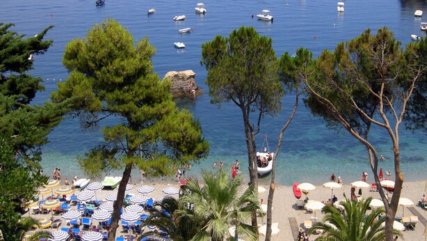 Una playa con aguas cristalinas, barcos y sombrillas.