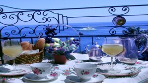 Una mesa dispuesta con una cesta de pan, una planta en maceta y un hervidor de agua, con vista al mar.