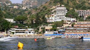 Un pueblo costero con una colina destacada, edificios y una zona de playa con barcos y sombrillas.
