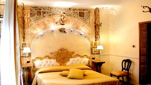Habitación de hotel con una cama grande, una silla y una pared decorativa con un arco de piedra.