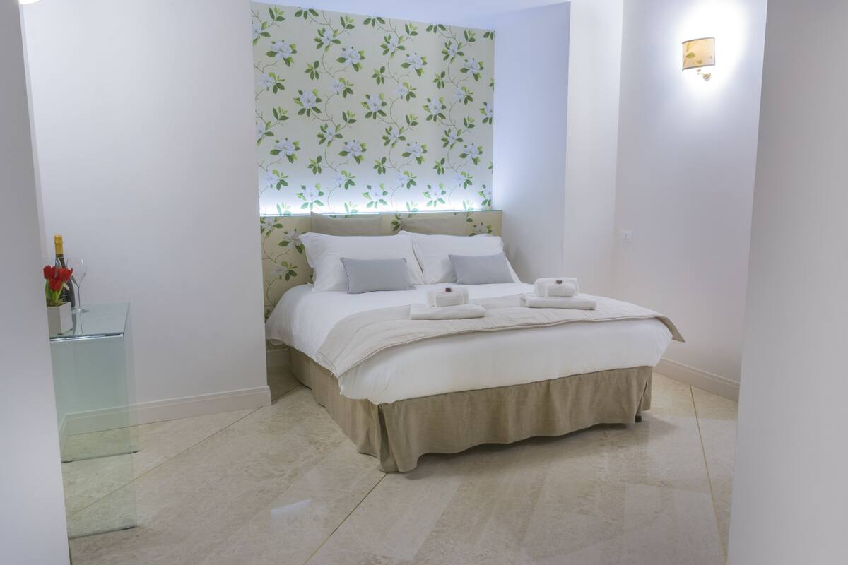 A neatly arranged bedroom with a bed, bedside table, and a wall-mounted light fixture.