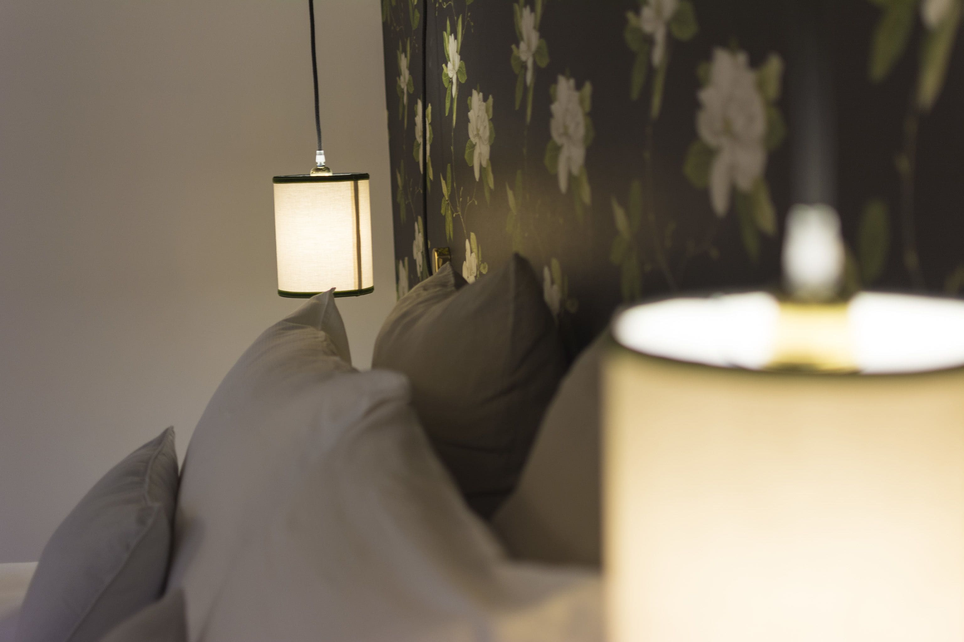 A bedroom with a bed, a bedside lamp, and a floral wallpaper.
