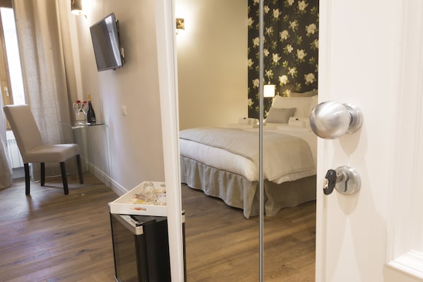 A hotel room with a bed, a TV mounted on the wall, a chair, and a small table with a bottle and glasses.