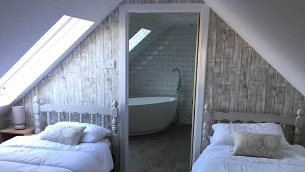 A bedroom with two beds, a skylight, and a bathroom with a bathtub. - Dunruadh Cottage (Alexandria)