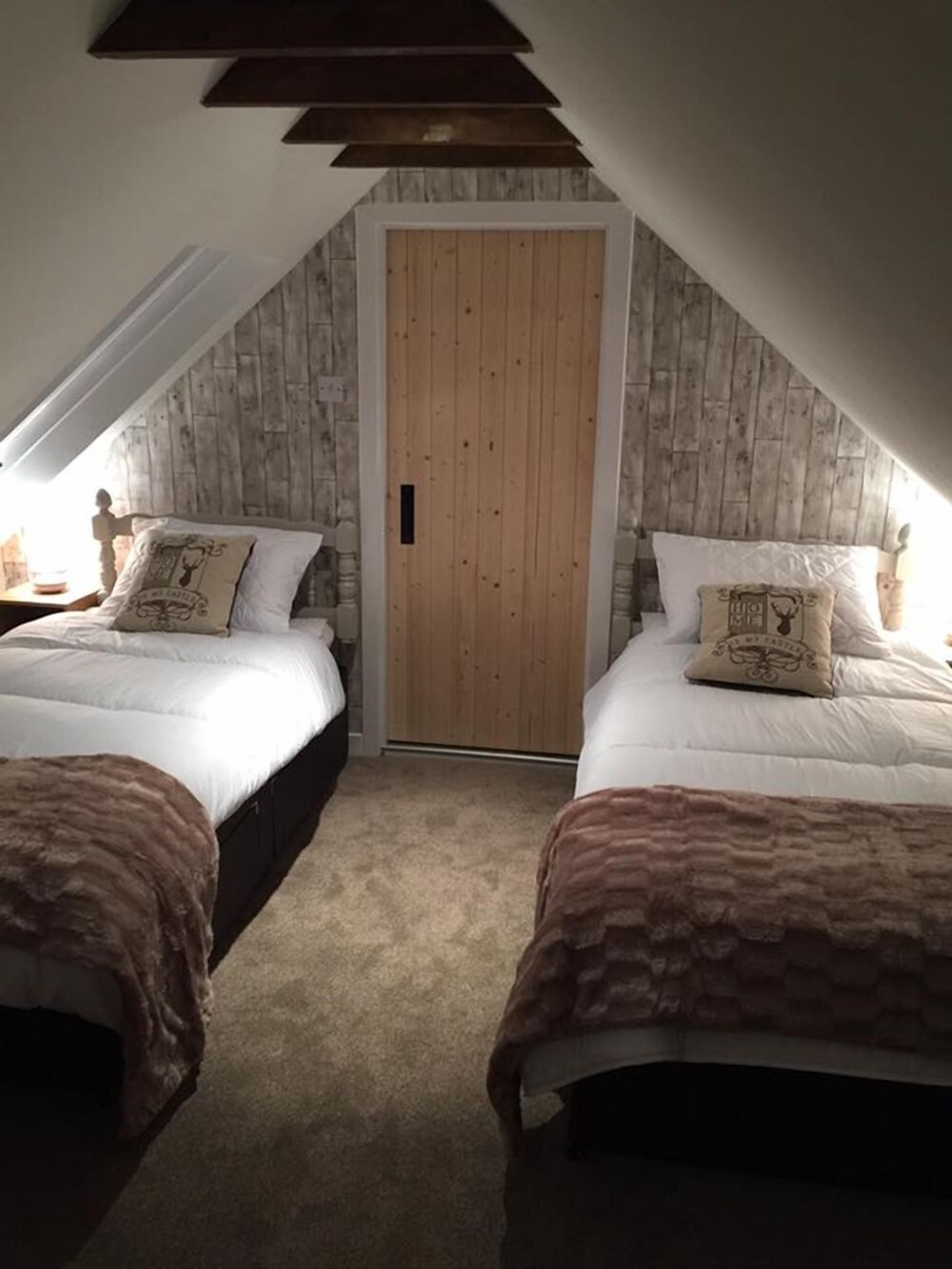 A bedroom with two beds, a wooden door, and a sloped ceiling.