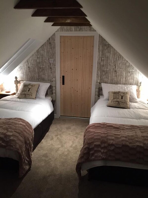 Quarto com duas camas, uma porta de madeira e teto inclinado.
